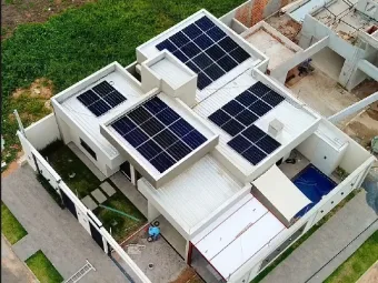 Casa branca vista de cima, com quatro conjuntos de módulos solares em telhados de alturas diferentes.
