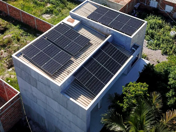 Sobrado de concreto visto de cima, com três conjuntos de módulos solares distribuídos pela laje e pelo telhado.