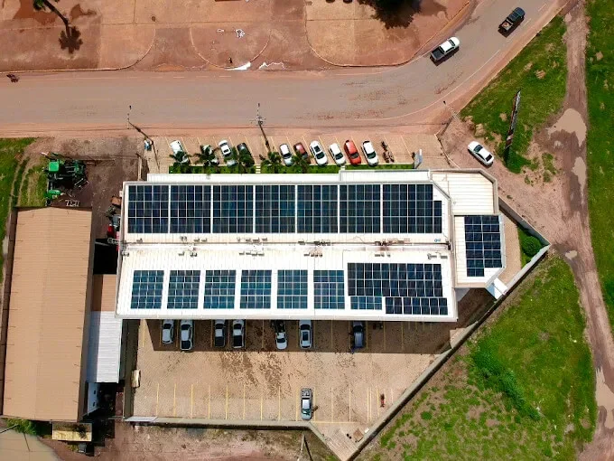 Prédio comercial visto de cima, com módulos solares cobrindo as duas águas do telhado e o estacionamento ao lado.