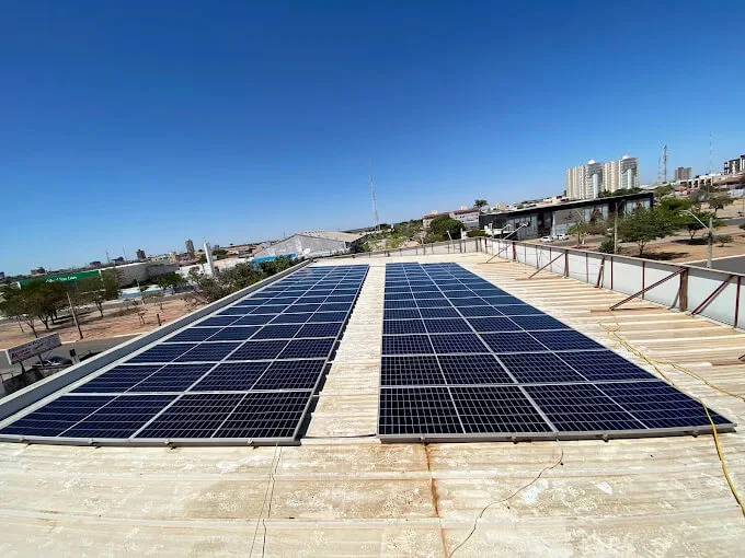 Fileiras de módulos solares instaladas sobre a laje de um prédio em Luís Eduardo Magalhães, com a cidade e o céu aberto ao fundo.